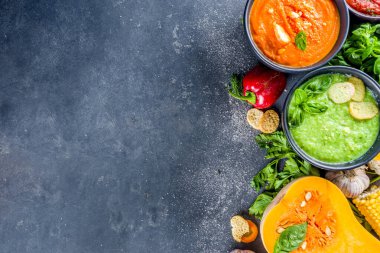 Farklı sonbahar çorbaları seti. Portakal kaselerinde çeşitli sebze çorbaları - mısır, patates, balkabağı, domates, kabak, brokoli kremalı çorba. Siyah beton arkaplanda üst görünüm kopyalama alanı