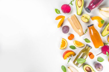 Meyve ve sebze püresi konsepti. Porsiyonlu meyve ve sebze suyu şişeleri beyaz masa arkasında taze malzemelerle bezenmiş.