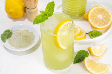 Buzlu Matcha Limonata kokteyli. Yeşil buzlu kibrit çayı, limon dilimleri ve beyaz arka planda taze nane ile karıştırılmış içecek. 