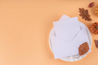 Sonbahar sofrası kurma, küçük balkabaklarıyla parti davetiyesi, güz yaprakları, tabak, çatal bıçak takımı ve bir davetiye veya selamlama ile birlikte zarf. Şükran Günü partisinin rahat arka plan fotokopi alanı