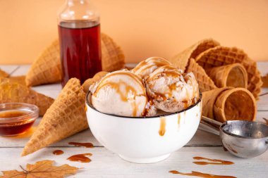 Lezzetli sonbahar akçaağaç şurubu dondurması. Akçaağaç şurubu tadında bir kase, üzerinde pekmezli çiseleme, akçaağaç yaprağı ve dondurma konileri olan dondurma, uzayı kopyala.