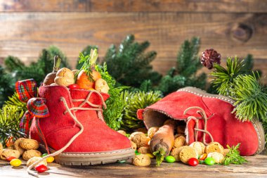 Sinterklaas, Saint Nicholas day background. Little kid red shoe with carrots and sweets, trooigoed, pepernoten, candy. Dutch Christmas holiday on cozy wooden background. 