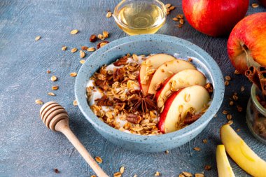 Sağlıklı sonbahar kahvaltısı ya da atıştırmalık, Yunan yoğurdu, granola, elma, bal ve cevizli kase, malzemeli mavi beton arka plan, kopyalama alanı