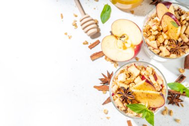 Apple Pie Granola Cheesecake, breakfast snack layered dessert with oat granola, cream cheese yogurt, honey, apple slices and cinnamon spices on white background copy space
