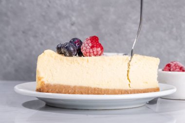 Tabakta peynirli kek dilimi, beyaz mermer zemin üzerinde ahududu. 