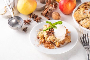  Elmalı gevrek tatlı, dondurmalı çıtır tart, kıtır kıtır hamurlu turta fırın tabağında ve tabakta, dondurma kepçesiyle beyaz mutfak masasında.