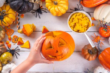 Balkabağı oyma Jack Feneri ile Cadılar Bayramı hazırlığı. Kadın, kadın ve çocuklar ellerini çerçeveye koyar, dekore eder, çizer ve korkunç Cadılar Bayramı partisini oyar.