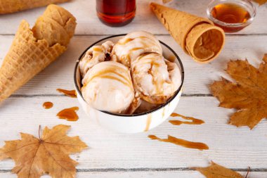 Lezzetli sonbahar akçaağaç şurubu dondurması. Akçaağaç şurubu tadında bir kase, üzerinde pekmezli çiseleme, akçaağaç yaprağı ve dondurma konileri olan dondurma, uzayı kopyala.