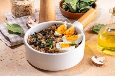 Lezzetli bir gecelik yulaf ezmesi. Ispanaklı, mantarlı ve yumurtalı lezzetli, şekersiz kahvaltı yulafları. Pişirmek için bej arka plan malzemeleri.