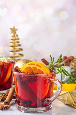 Geleneksel Noel aromalı şarap kokteyli, baharatlı kırmızı şarap içkisi, tarçın, portakal ve biberiye filizleri, Noel süslenmiş ahşap kaplama arka planda.