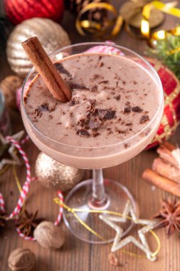 Baharatlı çikolatalı eggnog martini kokteyli, tarçın çubuğu, hindistan cevizi ve çikolata serpiştirilmiş, samimi bir Noel arkaplanı. 