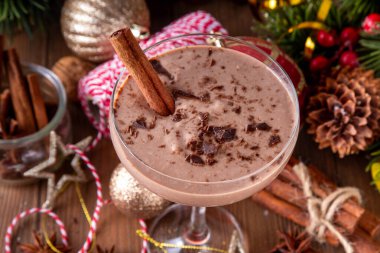 Baharatlı çikolatalı eggnog martini kokteyli, tarçın çubuğu, hindistan cevizi ve çikolata serpiştirilmiş, samimi bir Noel arkaplanı. 