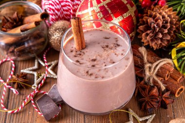 Baharatlı çikolatalı eggnog kokteyli, tarçın çubuğu, hindistan cevizi ve çikolata serpiştirilmiş, samimi bir Noel arkaplanı. 