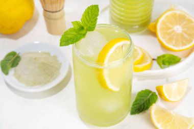 Buzlu Matcha Limonata kokteyli. Yeşil buzlu kibrit çayı, limon dilimleri ve beyaz arka planda taze nane ile karıştırılmış içecek. 