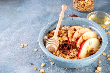 Sağlıklı sonbahar kahvaltısı ya da atıştırmalık, Yunan yoğurdu, granola, elma, bal ve cevizli kase, malzemeli mavi beton arka plan, kopyalama alanı