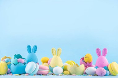 Tatlı ve parlak pastel renkli Paskalya yumurtaları ve tavşan arka planı. Pembe. Mavi, sarı renkli tavşanlar, yuvalarda ve yumurta kabuklarında çikolata yumurtaları, açık mavi arkaplanda şeker parçacıkları