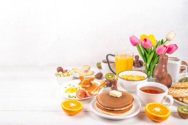 Paskalya tatili tatlı kahvaltı, brunch. Paskalya süslü Belçika waffle 'ları, krepler, kahvaltı gevrekleri ve süt, kızarmış yumurtalar kızarmış ekmek ve pastırma, Paskalya çikolatalı yumurtalar ve bahar çiçekleriyle birlikte tavşan.