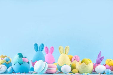 Tatlı ve parlak pastel renkli Paskalya yumurtaları ve tavşan arka planı. Pembe. Mavi, sarı renkli tavşanlar, yuvalarda ve yumurta kabuklarında çikolata yumurtaları, açık mavi arkaplanda şeker parçacıkları