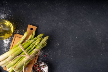 Çiğ organik kuşkonmaz mutfak masasının arka planında bir sürü ev yapımı yeşil kuşkonmaz pişirmeye ve kesme tahtasının üzerinde hazır. Yaz hasadı, yaz yemeği malzemeleri.