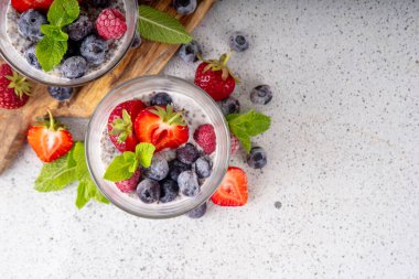 Taze dutlu Chia tohumu pudingi. Sağlıklı yaz kahvaltısı tatlı kremalı süt veya yoğurt, chia, çilek ve yabanmersini, beyaz masa arkaplan fotokopi alanı