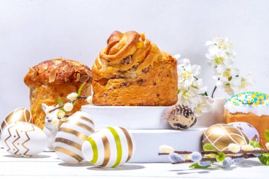 Paskalya yumurtaları, panettone, bahar çiçekleri ve ürün sergisi için kaide podyumları, beyaz ahşap arka planda Paskalya bayramı modeliyle mutlu Paskalya arkaplanları.