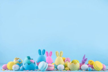 Tatlı ve parlak pastel renkli Paskalya yumurtaları ve tavşan arka planı. Pembe. Mavi, sarı renkli tavşanlar, yuvalarda ve yumurta kabuklarında çikolata yumurtaları, açık mavi arkaplanda şeker parçacıkları