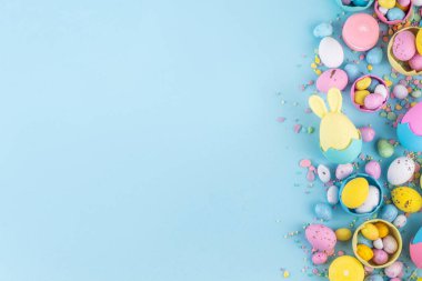 Tatlı ve parlak pastel renkli Paskalya yumurtaları ve tavşan arka planı. Pembe. Mavi, sarı renkli tavşanlar, yuvalarda ve yumurta kabuklarında çikolata yumurtaları, açık mavi arkaplanda şeker parçacıkları