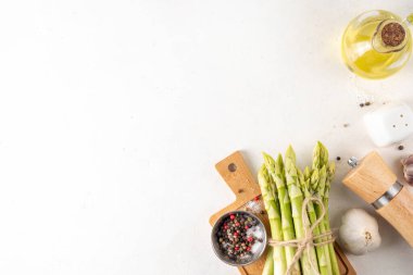 Çiğ organik kuşkonmaz mutfak masasının arka planında bir sürü ev yapımı yeşil kuşkonmaz pişirmeye ve kesme tahtasının üzerinde hazır. Yaz hasadı, yaz yemeği malzemeleri.