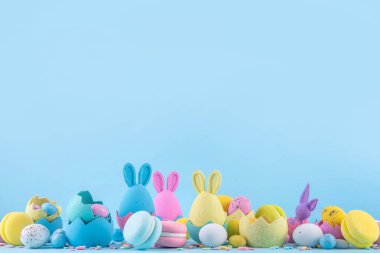 Tatlı ve parlak pastel renkli Paskalya yumurtaları ve tavşan arka planı. Pembe. Mavi, sarı renkli tavşanlar, yuvalarda ve yumurta kabuklarında çikolata yumurtaları, açık mavi arkaplanda şeker parçacıkları