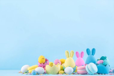 Tatlı ve parlak pastel renkli Paskalya yumurtaları ve tavşan arka planı. Pembe. Mavi, sarı renkli tavşanlar, yuvalarda ve yumurta kabuklarında çikolata yumurtaları, açık mavi arkaplanda şeker parçacıkları