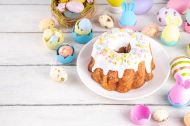 Geleneksel Paskalya pastası şekerleme ve şekerle süslenmiş, şenlikli ruh dekorasyonu ve çiçek buketiyle süslenmiş. Paskalya kutlamaları pastel renkli Paskalya yumurtaları ve tavşan tavşanlarıyla dolu tatil masası.