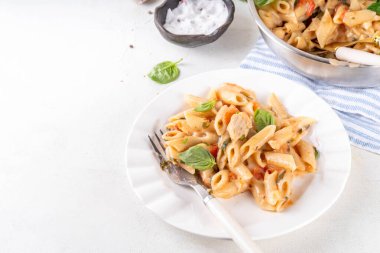 Son moda viral benimle tavuk makarnası evlen. Bir tencere yumuşak makarna ve kremalı ve peynirli sulu tavuk parçaları, sarımsaklı güneşte kurutulmuş domates sosu, nükteli fesleğen yaprağı, tabak ve demlikte.