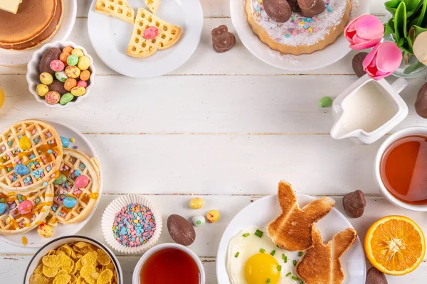 Paskalya tatili tatlı kahvaltı, brunch. Paskalya süslü Belçika waffle 'ları, krepler, kahvaltı gevrekleri ve süt, kızarmış yumurtalar kızarmış ekmek ve pastırma, Paskalya çikolatalı yumurtalar ve bahar çiçekleriyle birlikte tavşan.