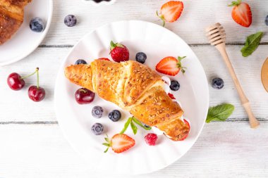 Krem şantili, taze meyve ve meyveli tatlı kahvaltı kruvasan sandviçi. Lezzetli bir yaz yemeği ya da içinde çilek, yabanmersini, kiraz, ahududu ve fındık bulunan taze kruvasanla atıştırmalık bir şeyler.