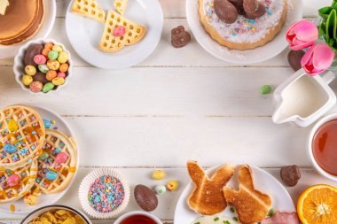Paskalya tatili tatlı kahvaltı, brunch. Paskalya süslü Belçika waffle 'ları, krepler, kahvaltı gevrekleri ve süt, kızarmış yumurtalar kızarmış ekmek ve pastırma, Paskalya çikolatalı yumurtalar ve bahar çiçekleriyle birlikte tavşan.