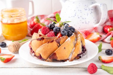 Taze meyve ve böğürtlenli yaz pastası. Geleneksel yuvarlak sünger keki, çilekli mevsimlik tatlı, ahududu, yabanmersini, bal ve şeker serpintileri, beyaz ahşap masa fotokopisi alanı