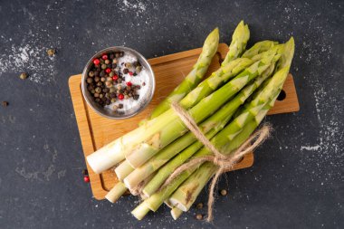 Çiğ organik kuşkonmaz mutfak masasının arka planında bir sürü ev yapımı yeşil kuşkonmaz pişirmeye ve kesme tahtasının üzerinde hazır. Yaz hasadı, yaz yemeği malzemeleri.