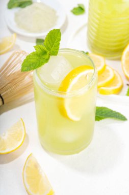 Buzlu Matcha Limonata kokteyli. Yeşil buzlu kibrit çayı, limon dilimleri ve beyaz arka planda taze nane ile karıştırılmış içecek.