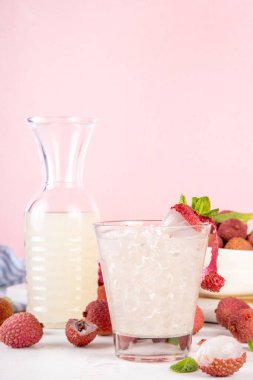 Meyve aromalı margarita veya limonata kokteyli. Lezzetli alkollü içecek taze liçi, nane yaprağı, likör ve tatlı ekşi meyve suyu, beyaz pembe masa arkaplanında olgun çiğ liçi meyveleri, kopyalama alanı