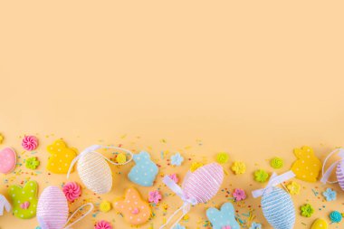 Tatlı ve parlak pastel renkli Paskalya yumurtaları ve tavşan arka planı. Pembe. Mavi, sarı renkli tavşanlar, yumurtalar ve çiçekler açık sarı zemin üzerine şeker serpiştirilmiş.