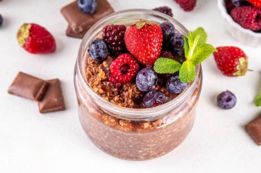 Çikolatalı Yulaf ezmesi, çikolata soslu, fındıklı ve taze dutlu, beyaz mutfak masasında yuvarlanmış yulaf, ahududu, yaban mersini, çilekli