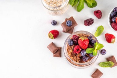 Çikolatalı Yulaf ezmesi, çikolata soslu, fındıklı ve taze dutlu, beyaz mutfak masasında yuvarlanmış yulaf, ahududu, yaban mersini, çilekli