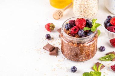 Çikolatalı Yulaf ezmesi, çikolata soslu, fındıklı ve taze dutlu, beyaz mutfak masasında yuvarlanmış yulaf, ahududu, yaban mersini, çilekli
