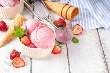 Yaz ferahlatıcı soğuk tatlı, lezzetli ve aromatik çilekli dondurma, seramik kasede ev yapımı meyve şerbeti, taze çilekler, beyaz ahşap arka planda dondurma külahları.