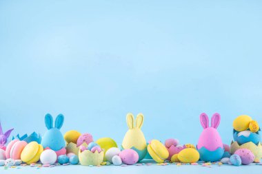 Tatlı ve parlak pastel renkli Paskalya yumurtaları ve tavşan arka planı. Pembe. Mavi, sarı renkli tavşanlar, yuvalarda ve yumurta kabuklarında çikolata yumurtaları, açık mavi arkaplanda şeker parçacıkları