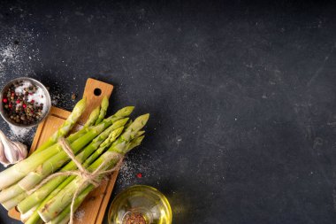 Çiğ organik kuşkonmaz mutfak masasının arka planında bir sürü ev yapımı yeşil kuşkonmaz pişirmeye ve kesme tahtasının üzerinde hazır. Yaz hasadı, yaz yemeği malzemeleri.