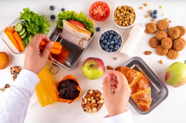 Çocuklar için sağlıklı okul yemekleri. Okul için ev yapımı sağlıklı beslenme çantası hazırlıyorum. Sandviç, meyve, meyve, meyve suyu, fındık. Beyaz masada beslenme çantalı malzemeler ve yiyecekler.