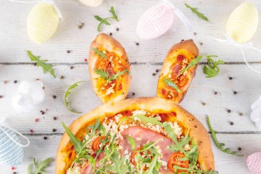 Yaratıcı, tavşan kulaklı Paskalya Tavşanı şekilli pizza yaptı. Domatesli Paskalya bayramı pizzası, pastırma ve taze roka, dekorlu - tavşanlar, Paskalya yumurtaları kopyalama alanı