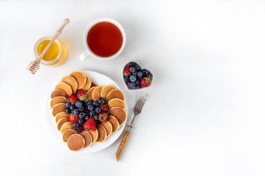 Sevgililer Günü tatlı kahvaltı krepleri kalp şeklinde serilmiş, taze ahududu, yabanmersini ve bal ile çay fincanı ve çaydanlık ile, kopyalama alanı ile