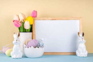 Bahar Paskalya bayramı masası boyalı Paskalya yumurtaları, bahar çiçekleri buketi, dekoratif tavşanlar, beyaz mutfak arka planında